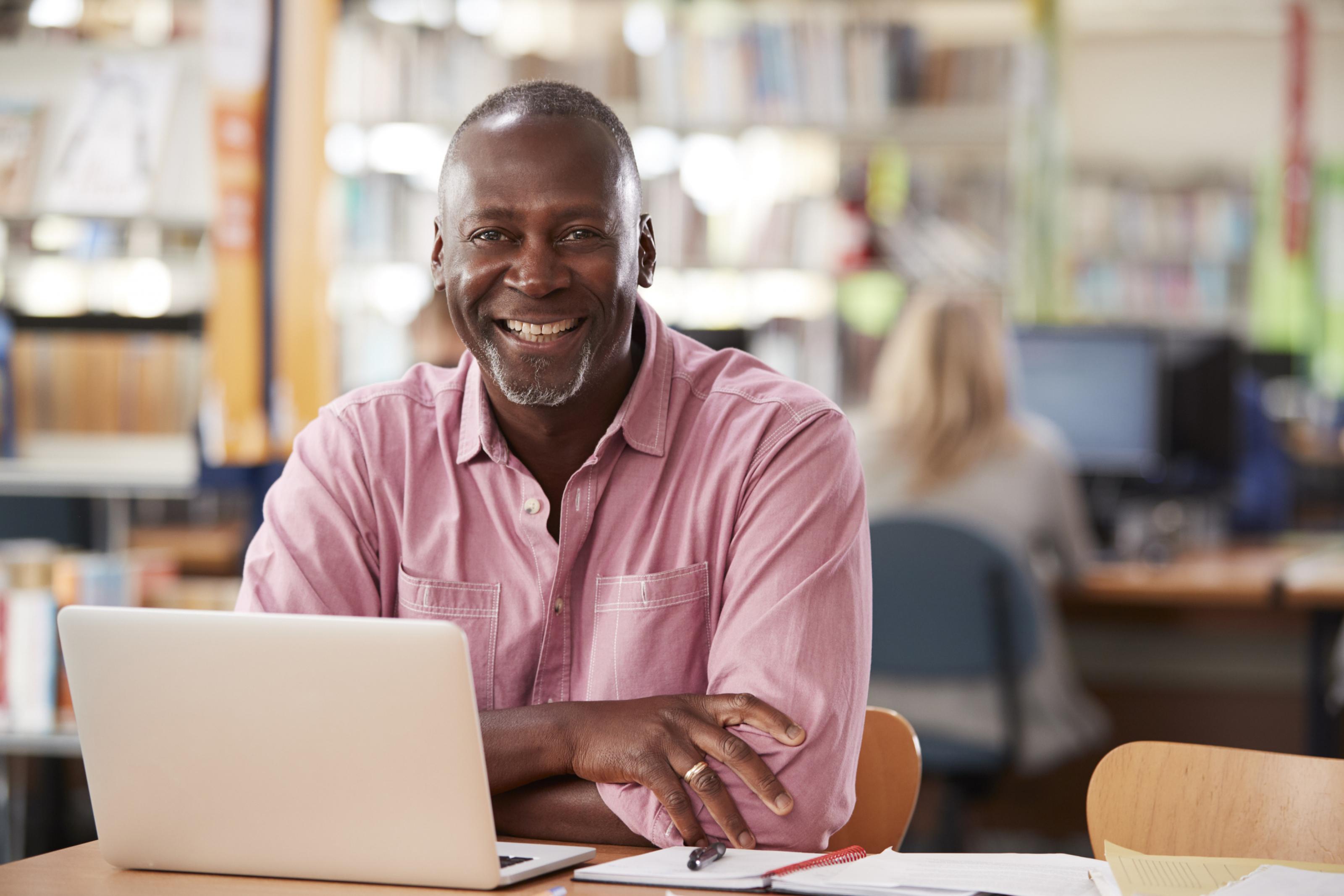 Dark-skinned man seated at a computer, smiling at the camera
